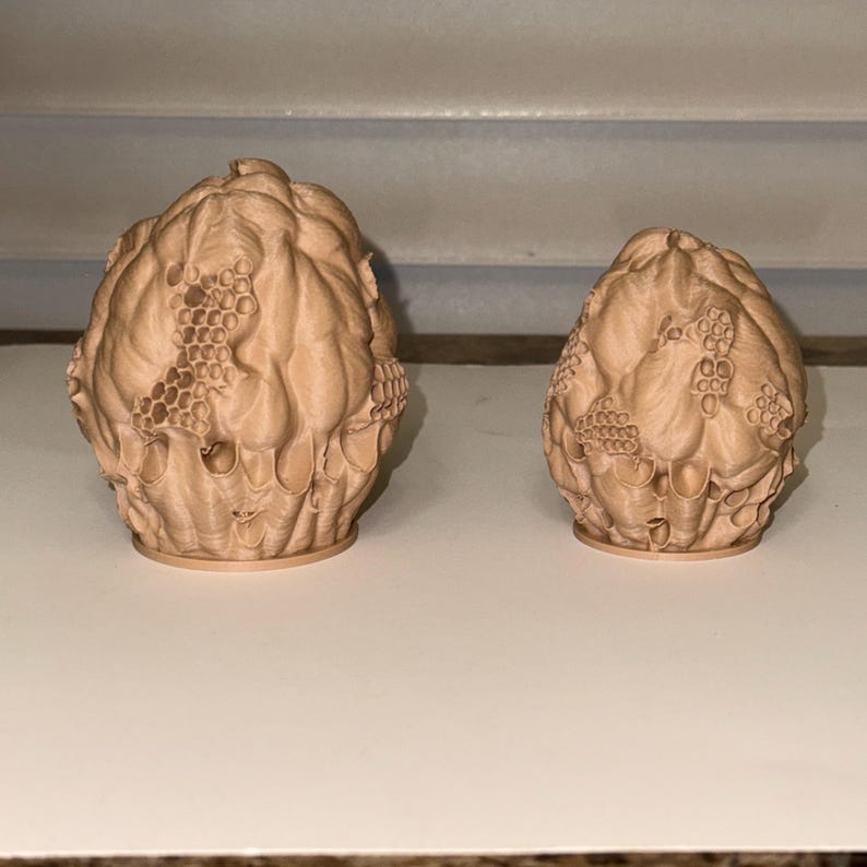 Peut inclure: Deux objets d&eacute;coratifs beiges imprim&eacute;s en 3D. Les objets pr&eacute;sentent un design textur&eacute; et organique avec un motif en nid d'abeille. Le plus grand objet est &agrave; gauche et le plus petit &agrave; droite. Les objets sont pos&eacute;s sur une surface blanche.