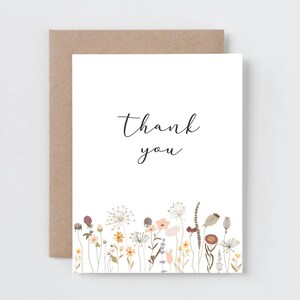 May include: A white card with the text "Thank you" in black cursive script. The card is decorated with a border of small, colorful flowers.