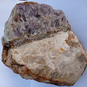 Peut inclure: Une grosse roche d'améthyste violette brute avec une base blanche et brune. Les cristaux d'améthyste sont regroupés et ont un aspect naturel et brut.