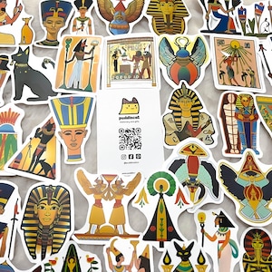 May include: A collection of colourful stickers featuring Egyptian-themed imagery, including pharaohs, scarabs, and hieroglyphics. The stickers are printed on white paper and have a glossy finish.