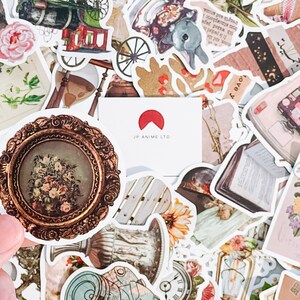 May include: A collection of vintage-style stickers with various designs, including floral arrangements, antique frames, a cat, a train, and a bunny. The stickers are in shades of brown, pink, and cream, with the text "JP ANIME LTD" on a white card.