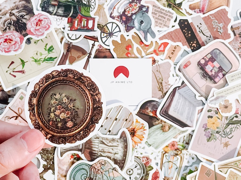 May include: A collection of vintage-style stickers with various designs, including floral arrangements, antique frames, a cat, a train, and a bunny. The stickers are in shades of brown, pink, and cream, with the text "JP ANIME LTD" on a white card.