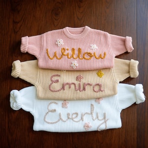 May include: Three knitted jumpers with embroidered names, "Willow", "Emira", and "Everly", each with small flower accents.