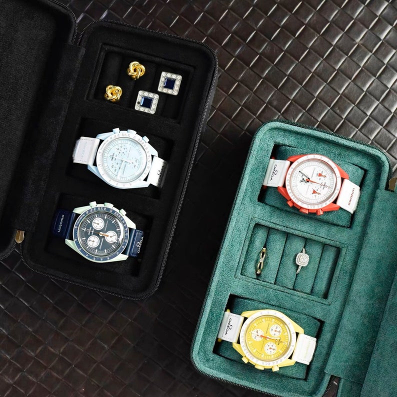 Op de afbeelding: Drie horlogedozen met verschillende horloges en sieraden. De dozen zijn gevoerd met groen vilt en hebben een zwarte buitenkant. De horloges hebben witte, rode en gele wijzerplaten.