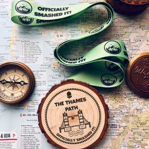 Peut inclure: Un ruban vert et noir avec le texte "Officially Smashed It!" et un graphique de chaîne de montagnes. Un rond en bois avec le texte "The Thames Path" et un graphique du Tower Bridge. Le texte "Officially Smashed It!" est également sur le rond en bois. Les articles sont sur une carte de l'Écosse.