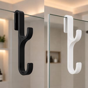 May include: Two shower door hooks, one black and one white, are displayed. The hooks are designed to hang over the top of a glass shower door. The hooks have a curved design with two lower hooks for hanging items like towels or robes.
