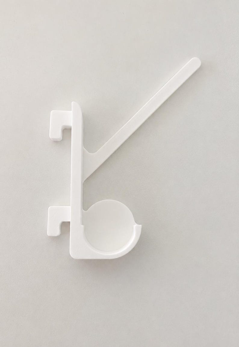 May include: A white plastic hook with a vertical spine, two rectangular mounting tabs on the left side, a circular cup-shaped holder at the bottom, and a long, angled support arm extending diagonally upward to the right.