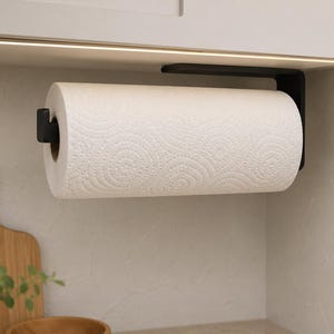 Könnte beinhalten: Ein mattschwarzer Papierrollenhalter aus Metall, der horizontal unter einem Schrank montiert ist. Der Halter verfügt über eine L-förmige Halterung und eine Endkappe, um eine Rolle weißes Küchenpapier mit kreisförmigem Muster zu sichern.