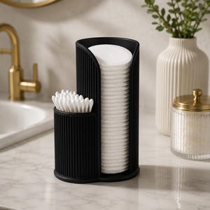 Könnte beinhalten: Ein schwarzer, gerippter Organizer für Badezimmerutensilien. Er hat zwei Fächer: eines für eine Stapel Wattepads, das andere für Wattestäbchen. Der Organizer steht auf einer Marmor-Arbeitsplatte, mit einer goldenen Armatur und dekorativen Elementen im Hintergrund.