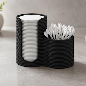 May include: A black ribbed bathroom organiser with two compartments. The taller compartment holds a stack of round white cotton pads, while the shorter compartment contains a cluster of white cotton buds with plastic stems.