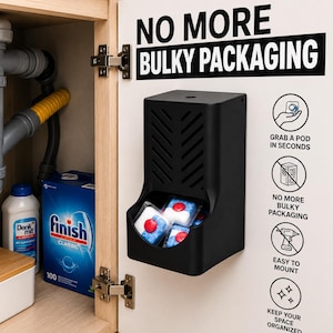 Op de afbeelding: Een zwarte wanddispenser voor vaatwastabletten bevestigd aan een kastdeur. De dispenser heeft een ontwerp met opening aan de bovenkant en een opening aan de voorzijde. De tekst op de deur luidt NO MORE BULKY PACKAGING en bevat iconen voor gebruik.