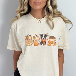 May include: A cream colored t-shirt with a graphic of a dog, a pumpkin spice latte, and a pumpkin spice coffee cup. The text on the coffee cup says "Pumpkin Spice Latte".
