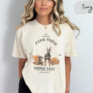 May include: A cream colored t-shirt with a graphic of two dogs and pumpkins. The text on the shirt reads "The Original Farm Fresh Pumpkin Patch Open Daily".