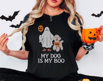 May include: Black t-shirt with a Halloween-themed graphic. The design features a ghost holding a balloon, a dog wearing a name tag, and the text "MY DOG IS MY BOO". The image also includes decorative bats and a pumpkin mug.