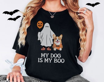 May include: Black t-shirt with a ghost holding a jack-o-lantern and a corgi wearing a bandana that says "NAME". The text on the shirt reads "My Dog Is My Boo."