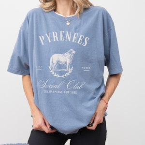 May include: A blue t-shirt with a white graphic of a sheep and the text "Pyrenees Social Club The Hamptons, New York"  EST 1983.