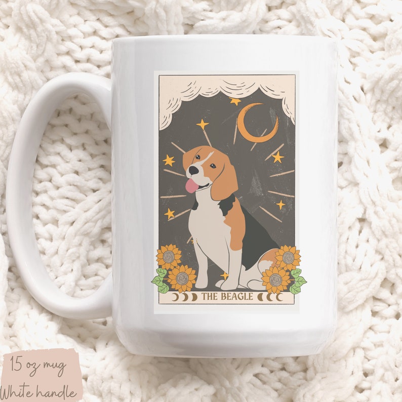 May include: White ceramic mug with a graphic of a beagle dog in a tarot card style illustration. The card has a dark brown background with stars, a crescent moon, and sunflowers. The text "THE BEAGLE" is printed below the dog.