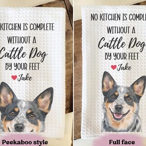 two towels with a humorous message about a dog. The towels feature a cute image of a dog's face and the text "No kitchen is complete without a Cattle Dog by your feet" along with a heart symbol and the name "Jake". The towels are labeled as "Peekaboo style" and "Full face" to indicate the style of the towel.