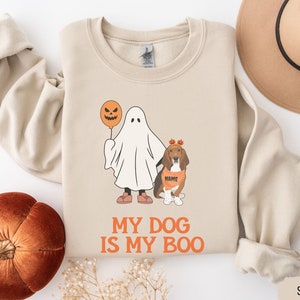 May include: Sand-colored sweatshirt with a Halloween-themed graphic. The design features a ghost holding a jack-o'-lantern balloon and a dog in a Halloween costume. The text "MY DOG IS MY BOO" is printed in orange.