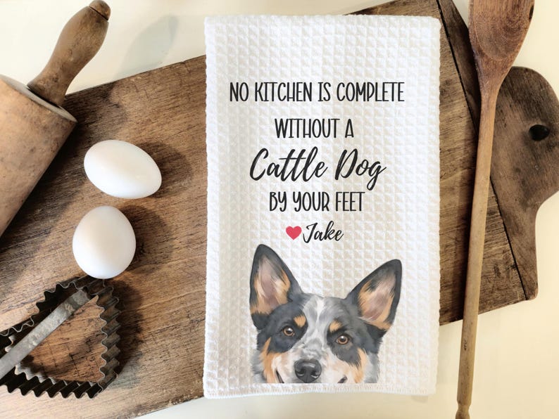 a kitchen towel with a dog image and text, along with some kitchen utensils such as a rolling pin and a wooden spoon.