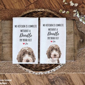 two white towels with a doodle of a dog's face and text printed on them, placed on a woven basket on a wooden surface.