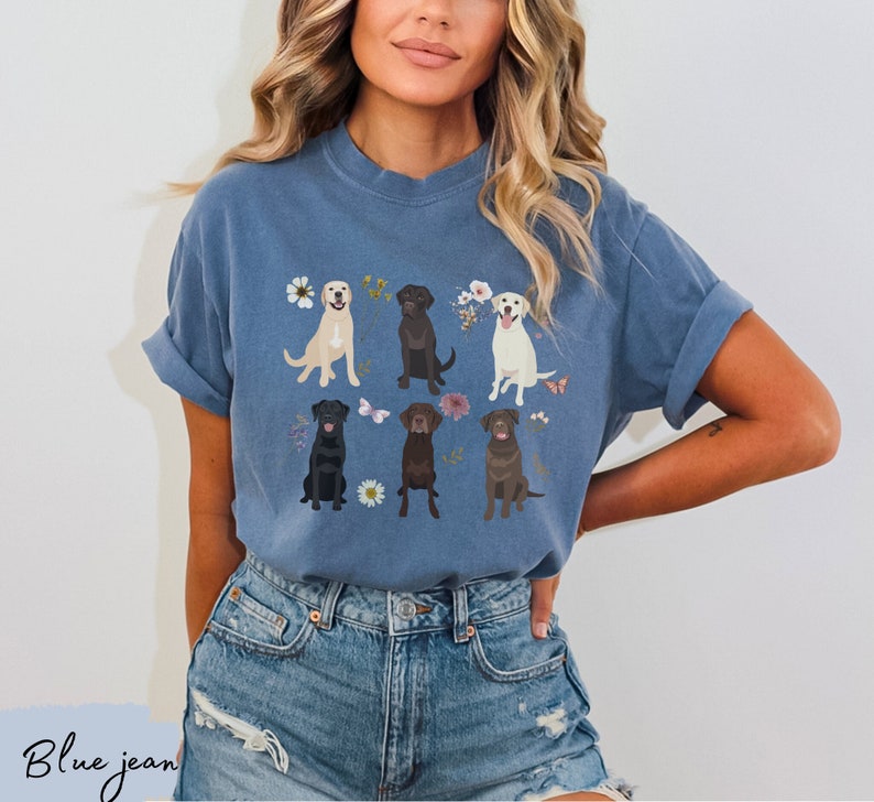 May include: A blue t-shirt with a graphic of six Labrador Retrievers in different colors, surrounded by flowers and butterflies.