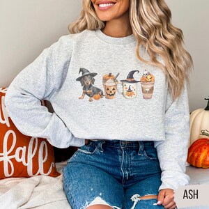 a woman sitting on a bed wearing a grey sweater with three witches on it