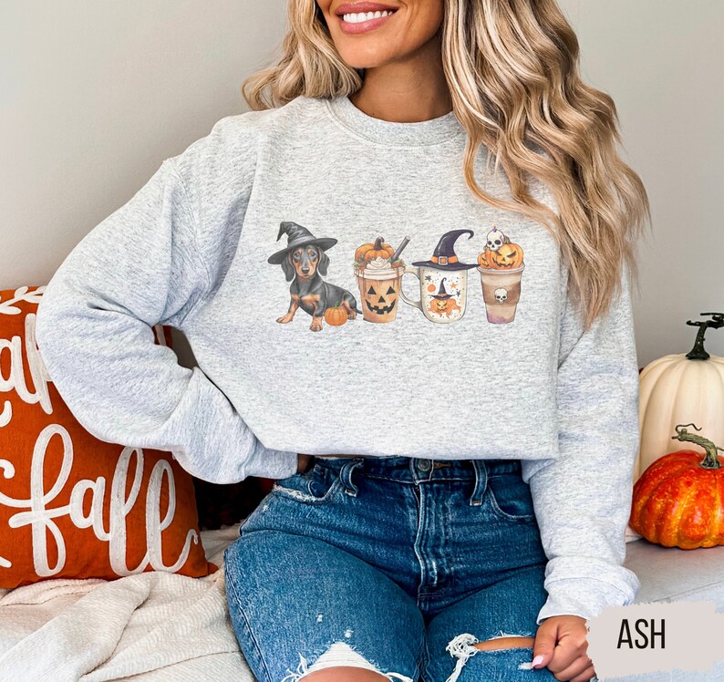 a woman sitting on a bed wearing a grey sweater with three witches on it