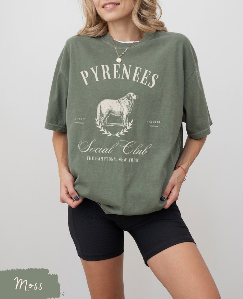 May include: A moss green t-shirt with a white graphic print of a dog and the text "Pyrenees Est 1983 Social Club The Hamptons, New York"