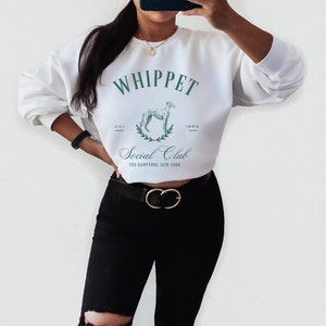Puede incluir: Sudadera blanca recortada con un gr&aacute;fico verde de un perro whippet y el texto "Whippet Social Club Est. 1993 The Hamptons, New York"