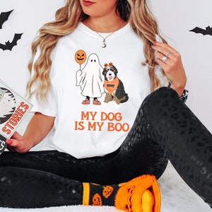 May include: White t-shirt with a ghost and dog illustration. The ghost is holding a jack-o-lantern balloon. The dog is wearing a bandana that says "NAME". The text on the shirt says "My Dog Is My Boo".