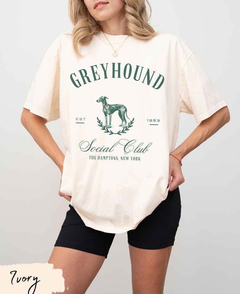 以下が含まれることがあります： クリーム色のTシャツに、緑色の犬のグラフィックプリントと「Greyhound Social Club, The Hamptons, New York」の文字がプリントされています。「Est. 1983」の文字もTシャツにプリントされています。