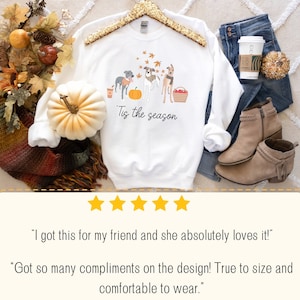 Puede incluir: Sudadera blanca con un gr&aacute;fico de tres perros y una calabaza. El texto "Tis the season" est&aacute; impreso debajo del gr&aacute;fico.