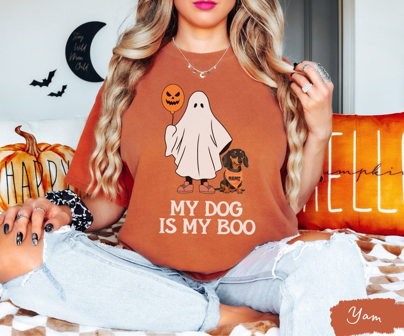 a woman sitting on a bed wearing a t - shirt that says my dog is