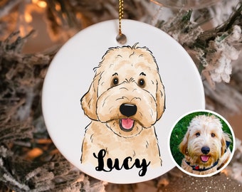 May include: A white ceramic Christmas ornament featuring a cartoon illustration of a light brown dog with the name "Lucy" written below. The ornament has a gold string for hanging.