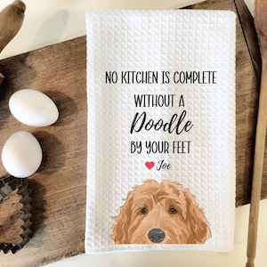 a kitchen towel with a dog illustration and a humorous message about cooking, placed on a wooden cutting board alongside kitchen utensils.