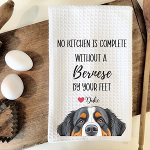 May include: White waffle-weave kitchen towel with the text "NO KITCHEN IS COMPLETE WITHOUT A Bernese BY YOUR FEET" and a Bernese Mountain Dog graphic. Includes a heart and the name "Duke".