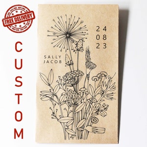 May include: A brown paper bag with a black and white illustration of a bouquet of wildflowers. The text "CUSTOM" is printed on the left side of the bag and "SALLY JACOB" is printed below the illustration. The date "24 08 23" is printed on the right side of the bag.