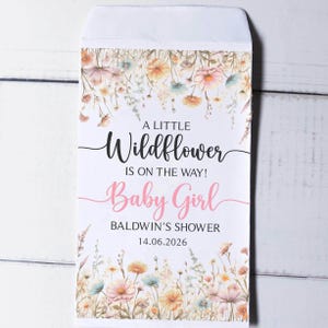 Op de afbeelding: Een witte envelop met een bloemenontwerp en de tekst "A Little Wildflower Is On The Way! Baby Girl". De envelop is versierd met aquarelbloemen in roze, geel en blauw, perfect voor een babyshower.