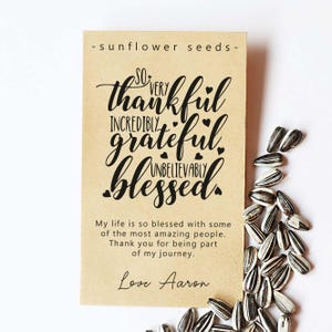 Op de afbeelding: Een bruin papieren zakje met zonnebloempitten met een boodschap die luidt: "So very thankful incredibly grateful unbelievably blessed." De boodschap is geschreven in zwarte cursieve letters met kleine hartjes rond de woorden. Het zakje bevat ook de tekst "My life is so blessed with some of the most amazing people. Thank you for being part of my journey. Love Aaron."