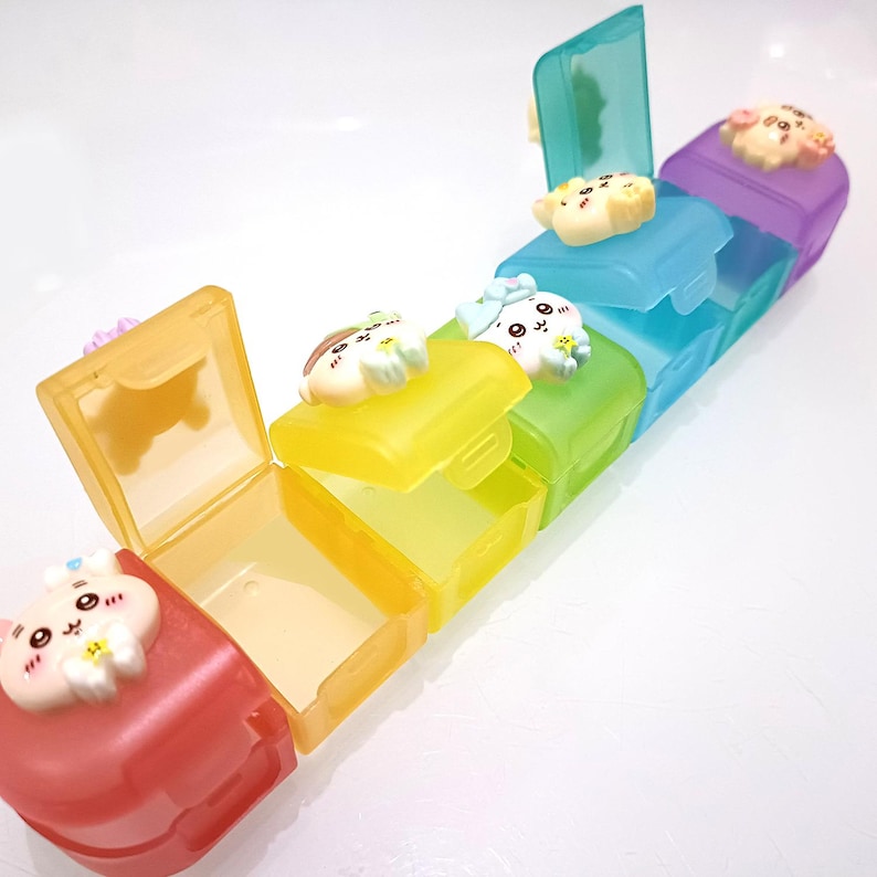 May include: A colorful, multi-compartment pill organizer with a hinged lid on each section. The sections are red, yellow, green, blue, and purple. Each lid is decorated with a cute cartoon animal.