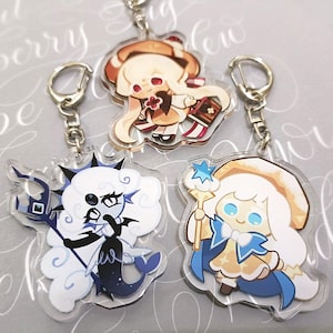 May include: Three acrylic keychains featuring cartoon characters. One character is in shades of brown, another in black and blue, and the third in white and blue. Each keychain has a silver-colored clasp.