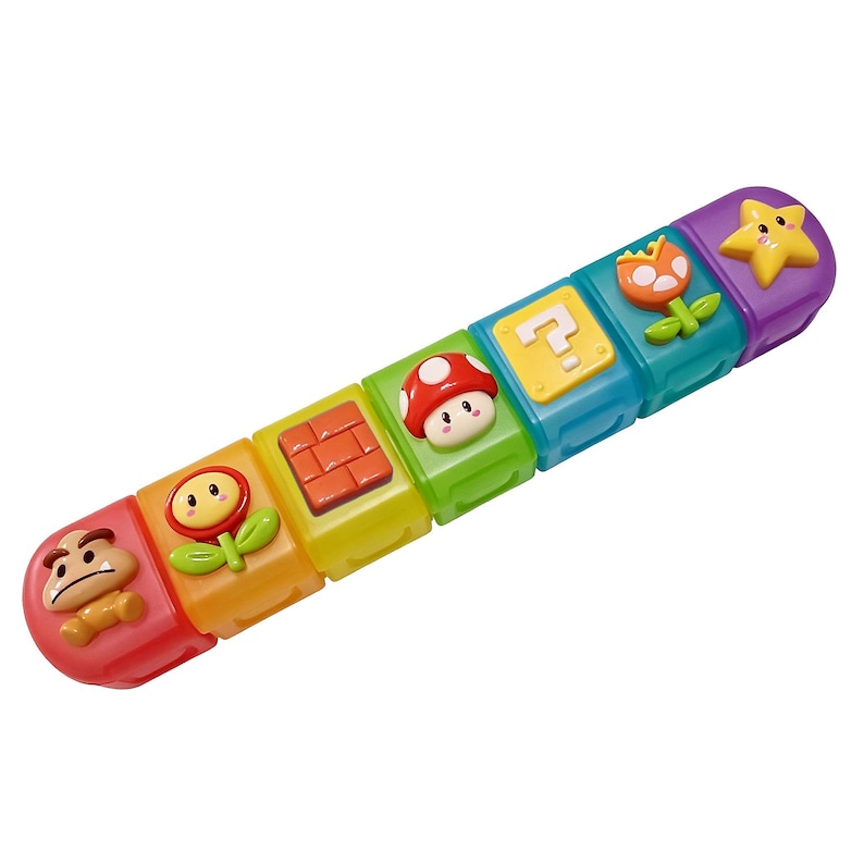 May include: A colorful toy featuring a series of connected blocks with various Super Mario-themed designs. The blocks include a Goomba, a flower, a brick, a mushroom, a question mark, another flower, and a star. The toy is made of plastic and has a rainbow color scheme.