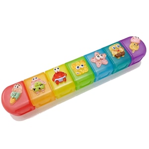 May include: A colorful, segmented pill organizer with seven compartments. Each compartment is a different color and features a raised, cartoon-like character, including a crab, starfish, and ice cream cone. The organizer is designed to hold pills or small items.