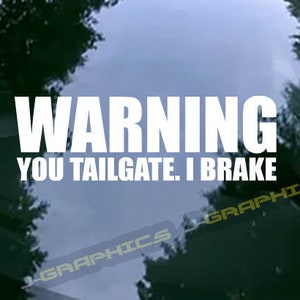 May include: White text on a window with the words "WARNING YOU TAILGATE. I BRAKE." The background is a view of trees and sky. The bottom right corner has the text "J-GRAPHICS".