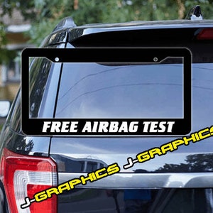 May include: Black license plate frame with white text that reads "FREE AIRBAG TEST". The frame is attached to the back of a black SUV.