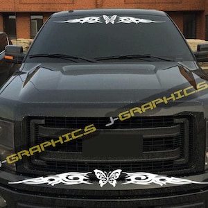 May include: Black truck with white tribal butterfly decals on the windshield and bumper. The front of the truck has a black grill and headlights. The text "J-GRAPHICS" is printed in yellow on the hood.