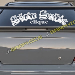 May include: A white vinyl decal with the words "Slow Subie Clique" in a stylized font on a gray car.