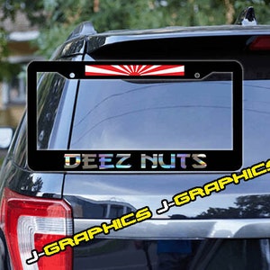 May include: Black license plate frame with a red, white, and blue rising sun design and the text "DEEZ NUTS" in a rainbow iridescent font.