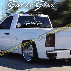 May include: A white pickup truck with tinted windows and chrome wheels. The text "God is Good" is displayed in a cursive font on the windshield and rear window. The truck has a lowered suspension and a black rear bumper.